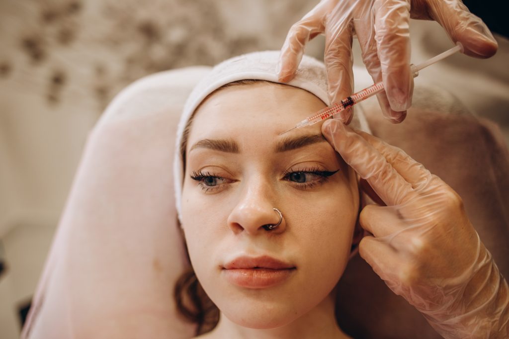 Portrait of young Caucasian woman getting botox cosmetic injection in forehead. Beautiful woman gets