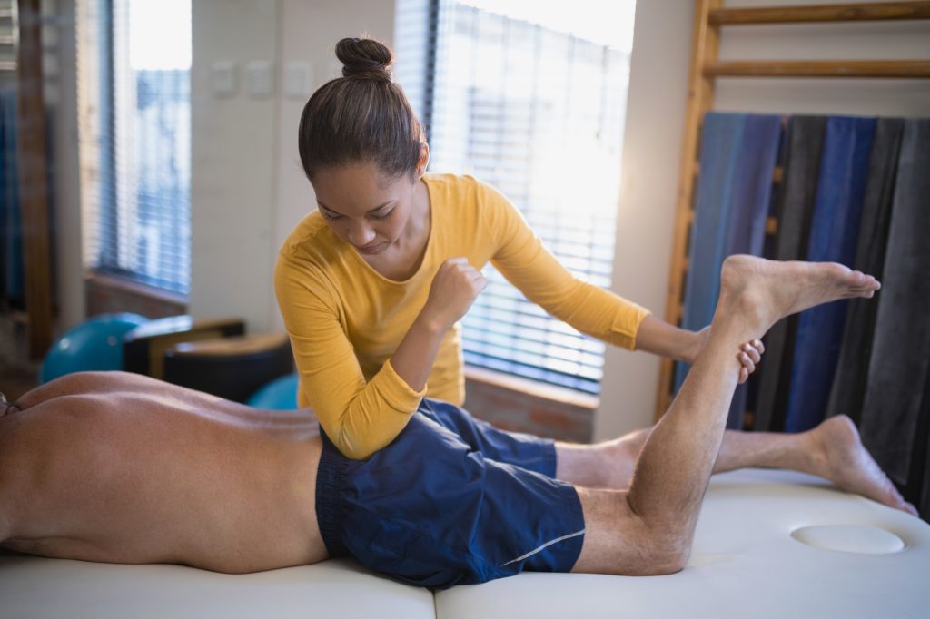 Young female therapist massaging buttocks of senior male patient
