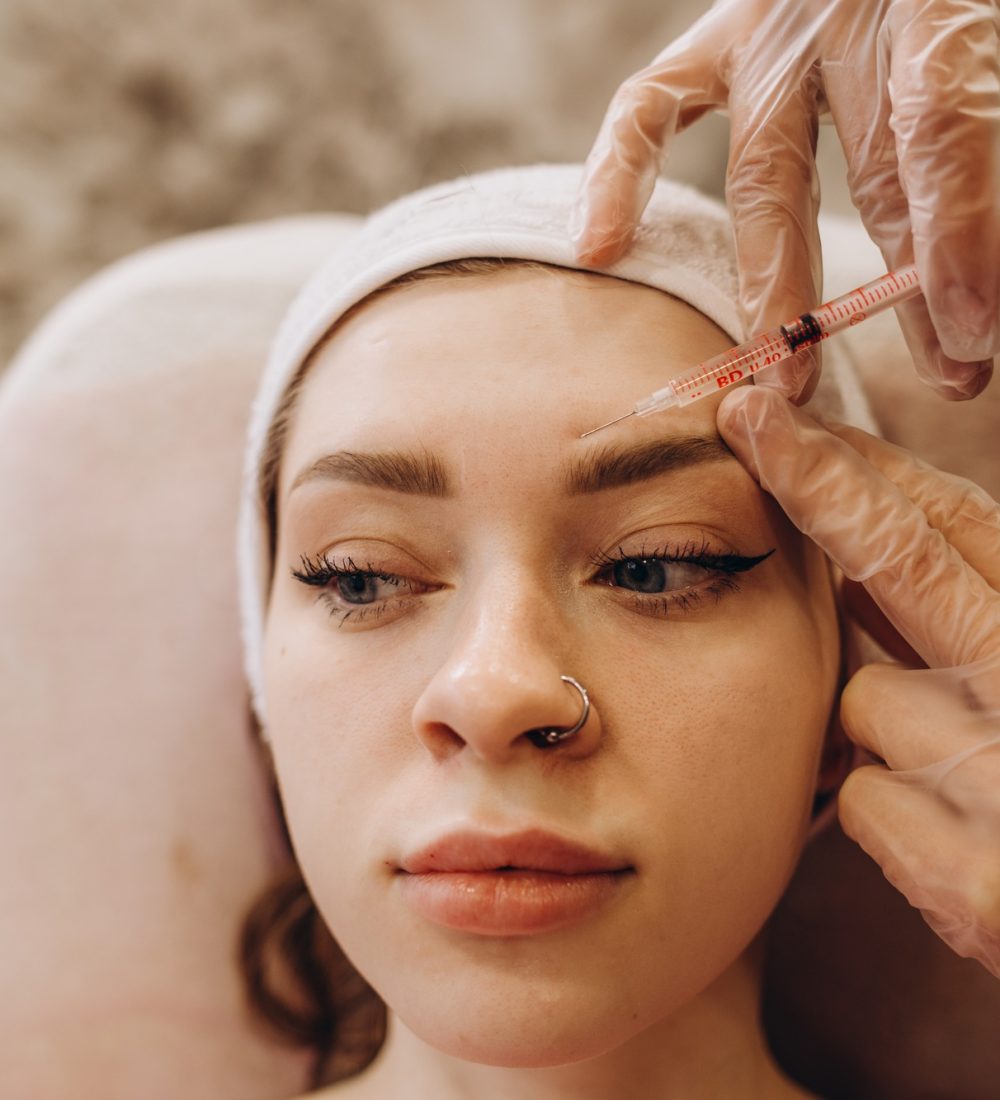 Portrait of young Caucasian woman getting botox cosmetic injection in forehead. Beautiful woman gets