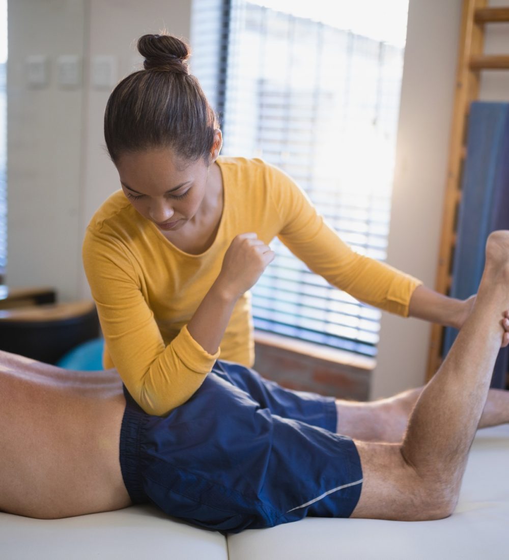 Young female therapist massaging buttocks of senior male patient
